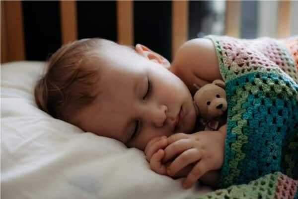 cute baby sleeps peacefully in crib with handle under his cheek